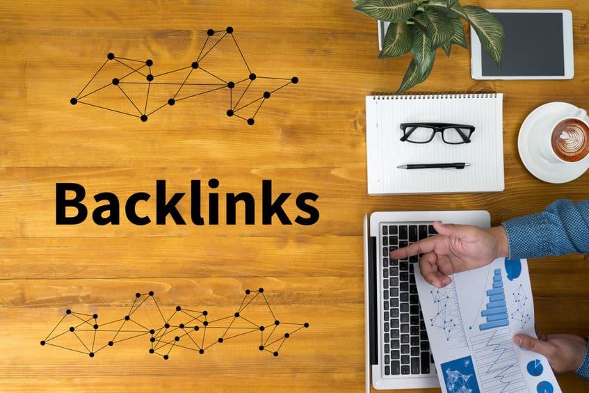 Un professionnel du marketing digital analysant des graphiques sur un ordinateur portable, avec le mot "Backlinks" affiché sur une table en bois, symbolisant les connexions SEO.