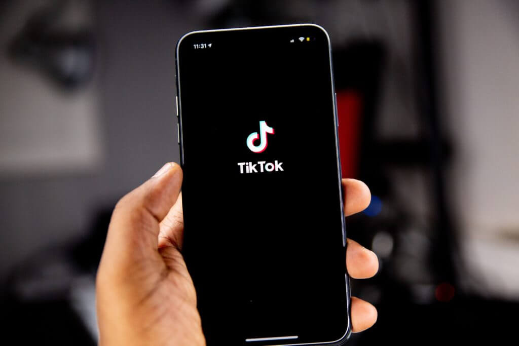 Main tenant un smartphone affichant le logo de l'application TikTok sur un écran noir, prêt à être lancé, avec un arrière-plan flou.