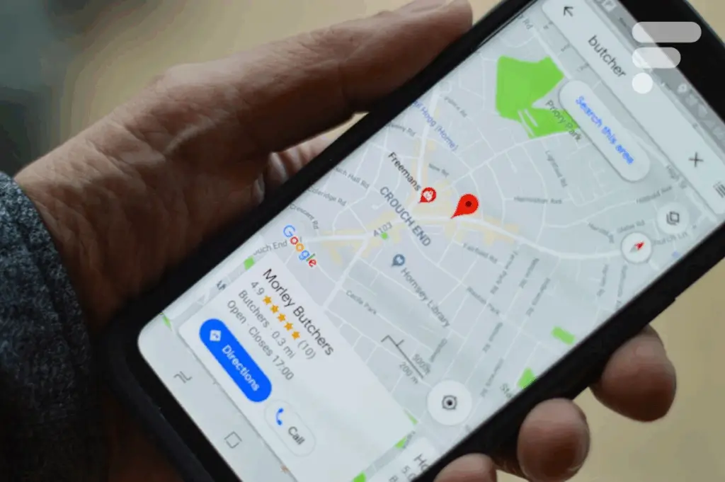 Main tenant un smartphone affichant Google Maps avec la fiche d’une boucherie mise en avant, incluant une note en étoiles et un bouton "Itinéraire"